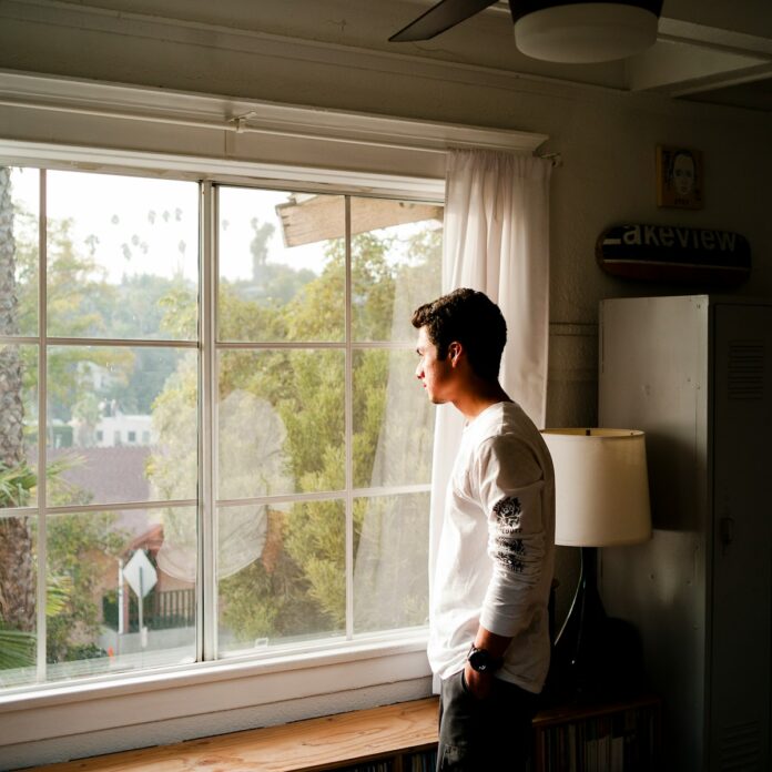 Photo by Hamish Duncan man wearing gray and black crew-neck shirt standing and looking out window